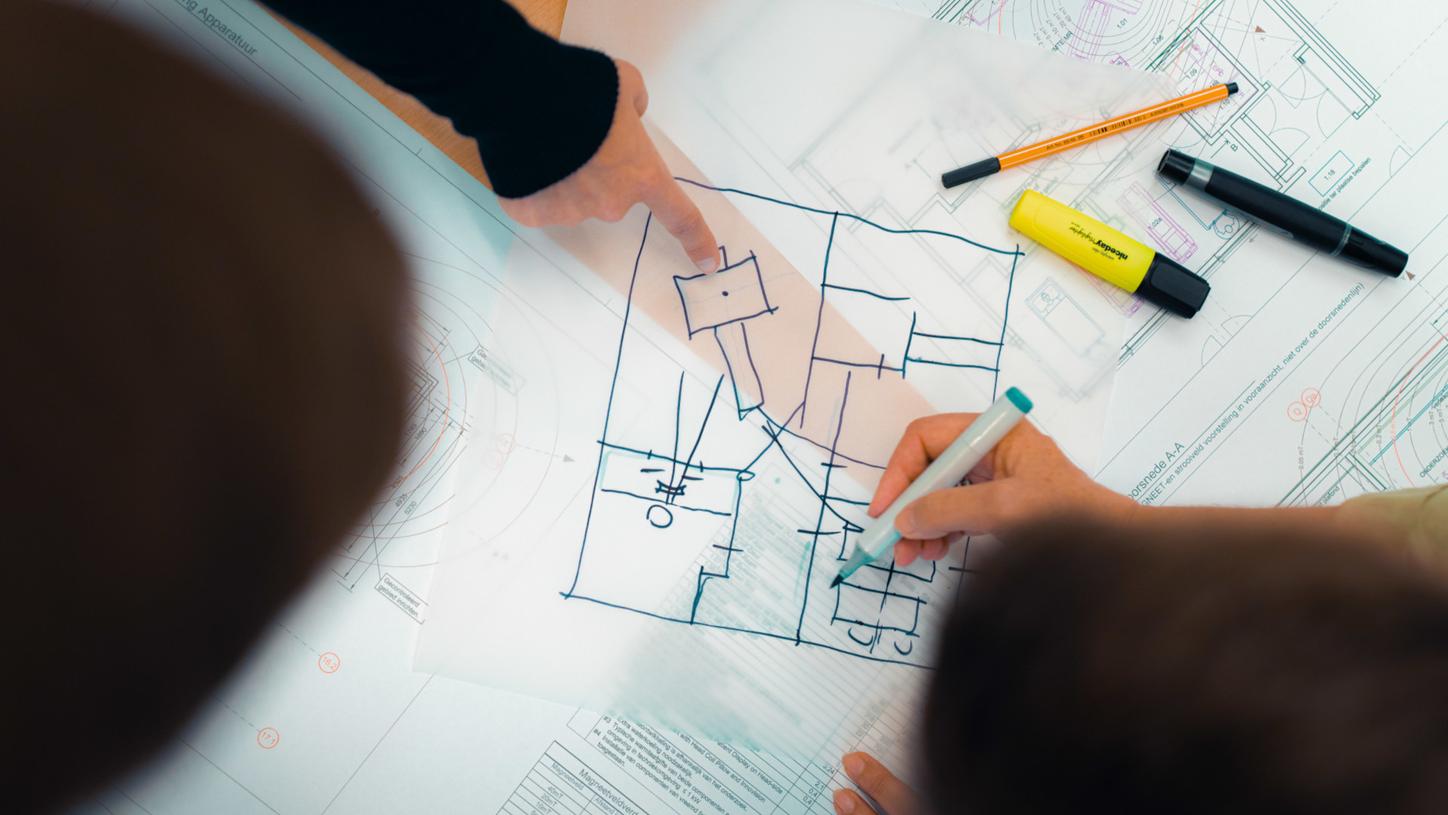 People reviewing and sketching a floor plan on architectural drawings.