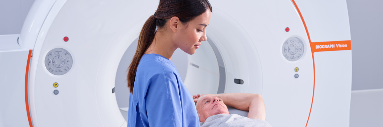 Male patient on Siemens Healthineers Biograph Vision PET/CT scanner bed with female tech.