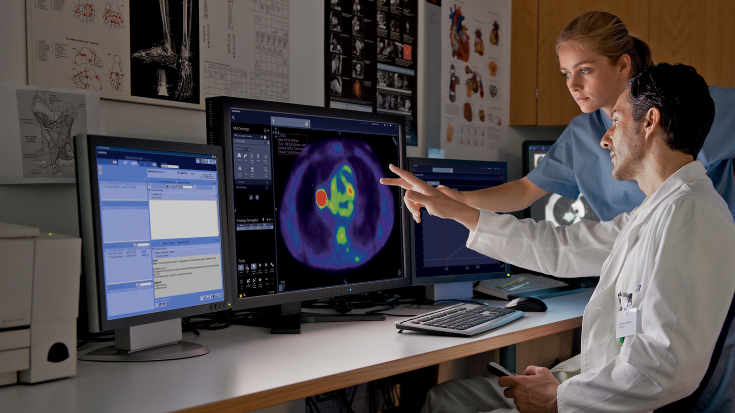 Male doctor and female tech reviewing imaging scan on monitor.