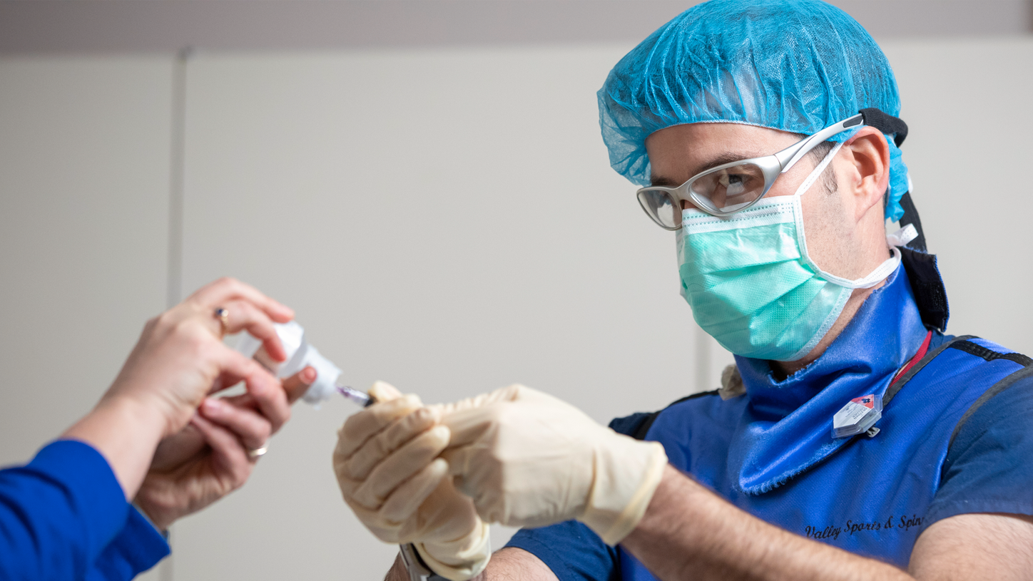 Ethan Colliver, DO, in a mask and scrubs, prepares a spinal injection.