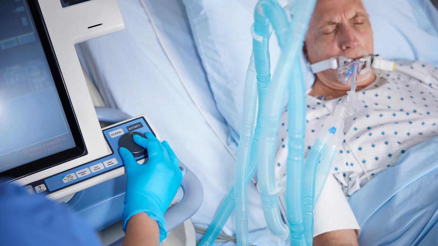 Clinician adjusting medical equipment while a patient receives respiratory support in a critical care setting