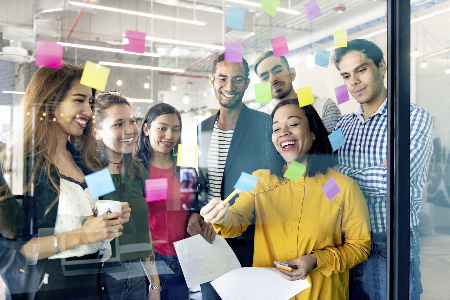 Young professionals planning tasks on glass wall with adhesive notes in co-working office