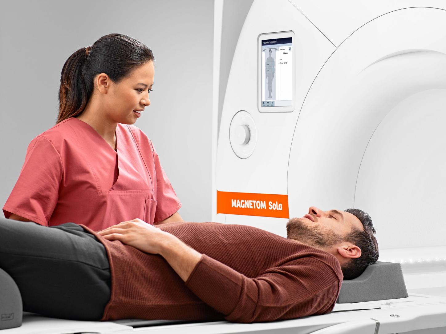 Application image, Magnetom Sola. Woman standing beside a man that lays in the machine.