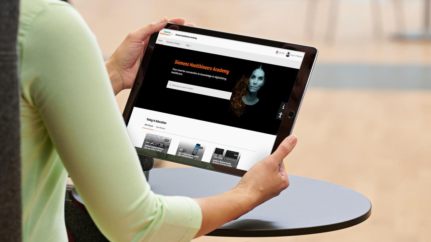 Woman sitting with tablet displaying Siemens Healthineers Academy homepage