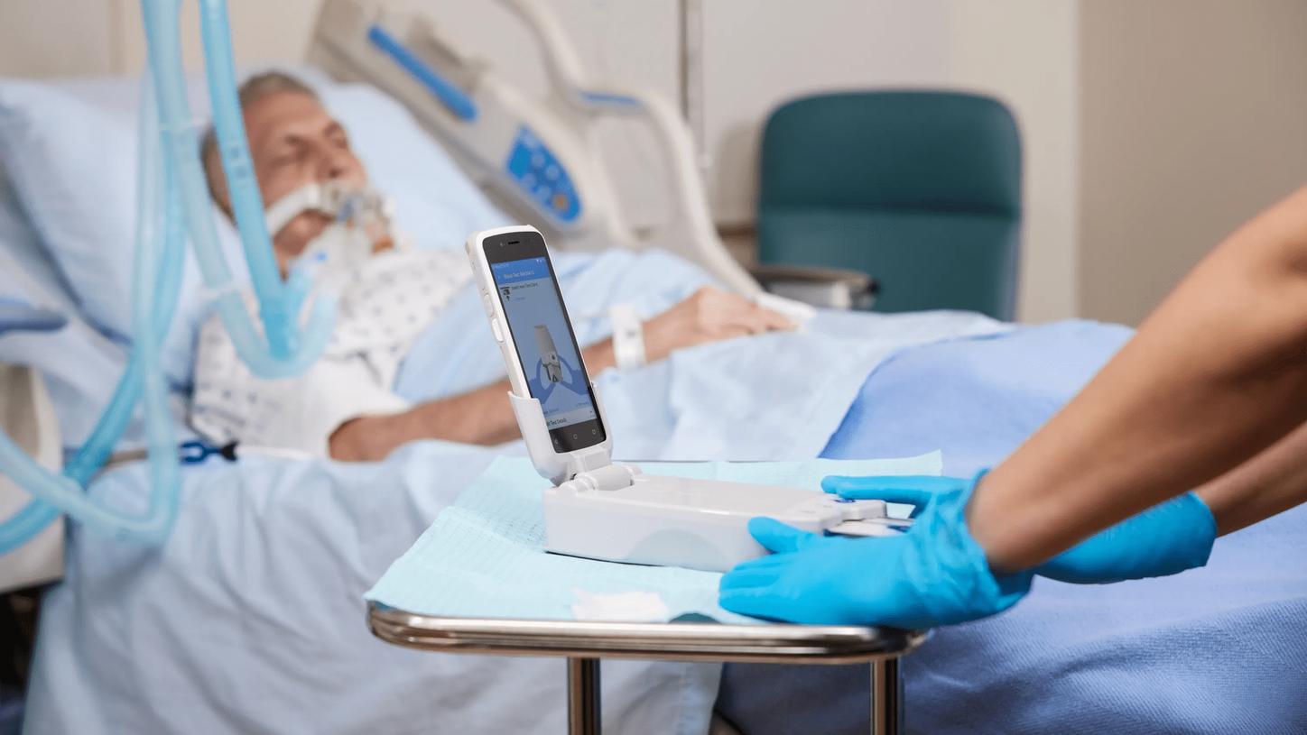 Clinician preparing point-of-care testing equipment beside a hospital patient receiving bedside care