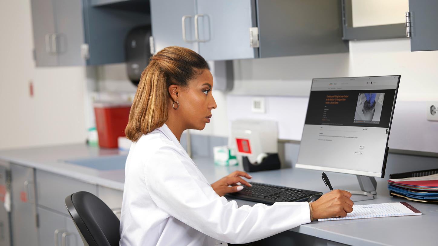 Lab technician completing online training at a computer in a clinical laboratory.