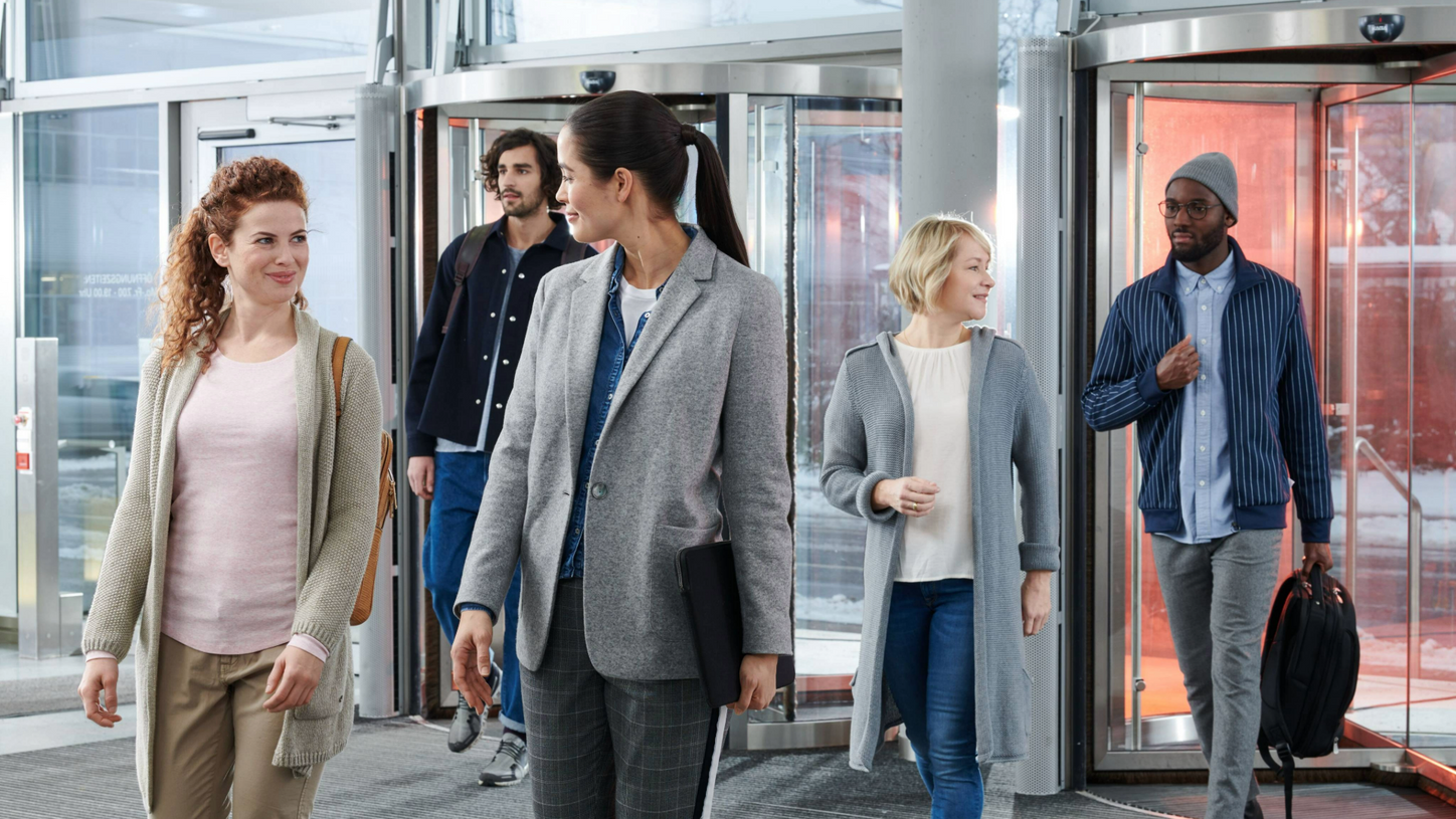 Fünf Kolleg*innen kommen durch Drehtür zur Arbeit.