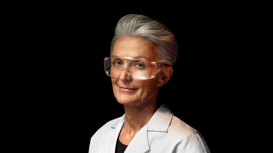 Scientist wearing safety glasses and white lab coat against black background