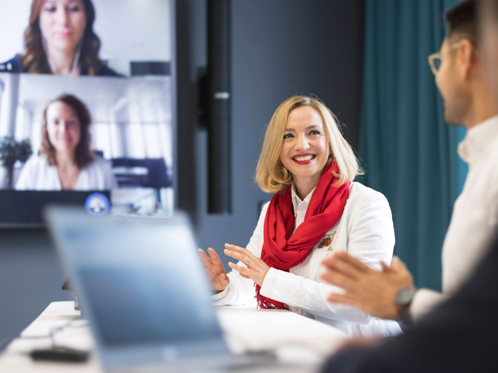 Mitarbeiterin nimmt an einem hybriden Meeting mit Kolleg*innen vor Ort und via Videocall teil.