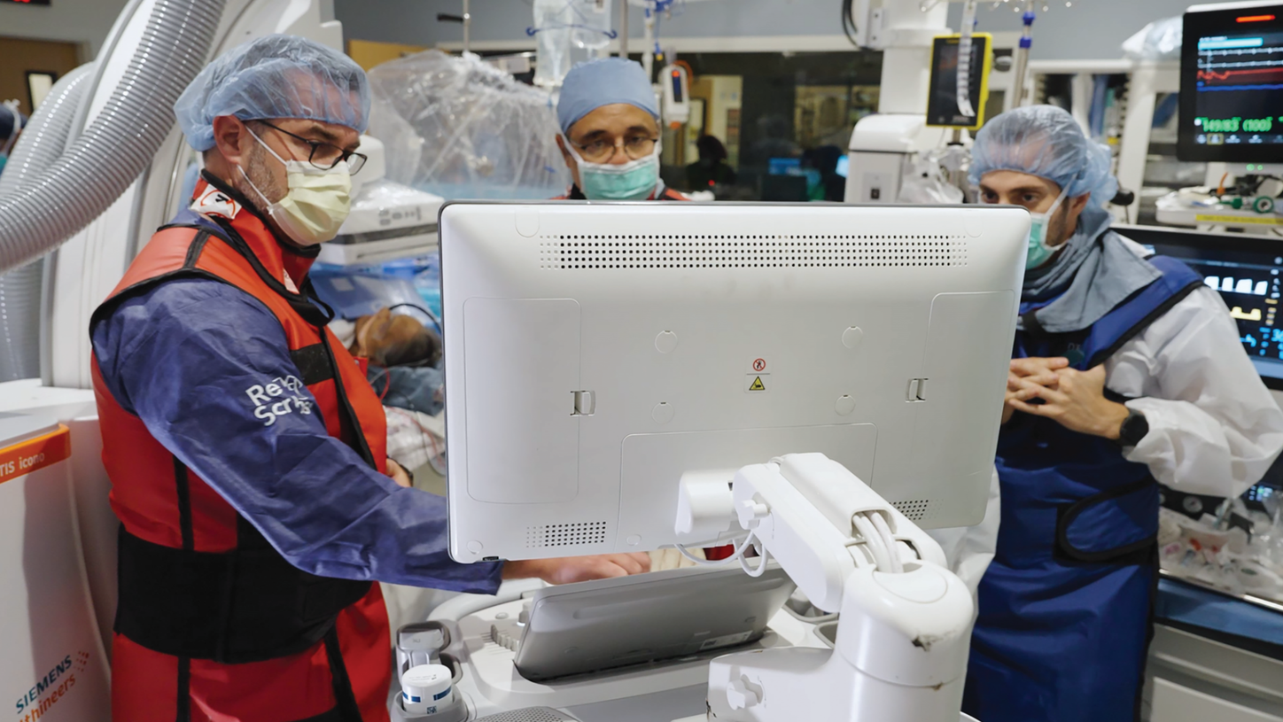 Several clinical workers in cleanroom gear — hairnets, face masks, and coveralls — working around an ACUSON Origin in sterile lab environment