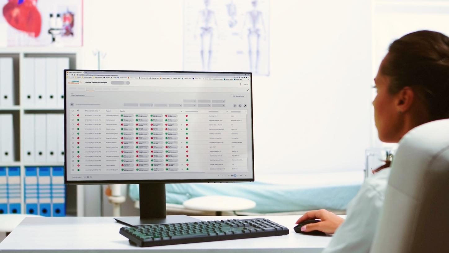 Healthcare professional reviewing point-of-care informatics dashboard and operational data on a desktop monitor