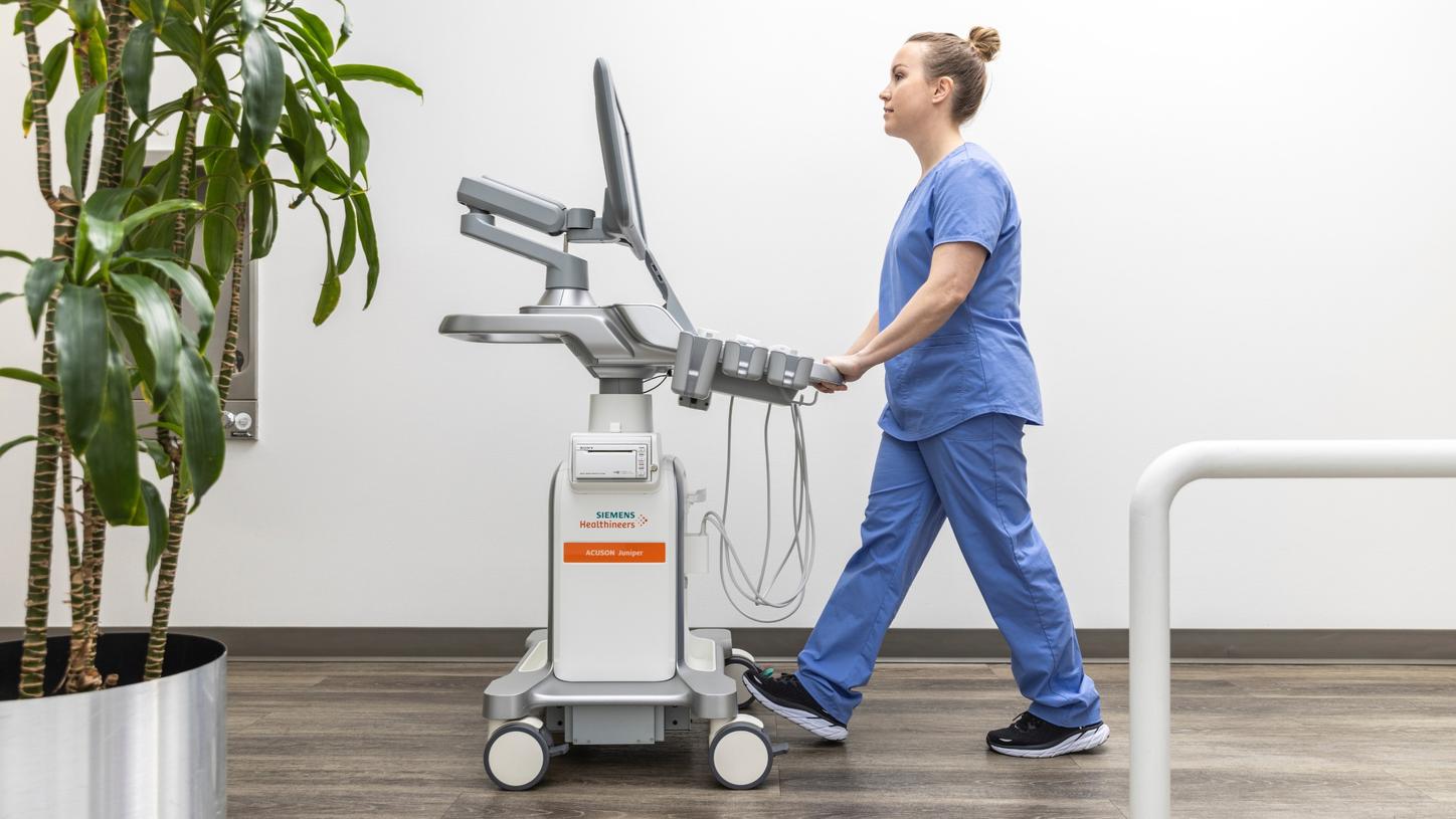 Sonographer pushing ACUSON Juniper ultrasound system down hallway