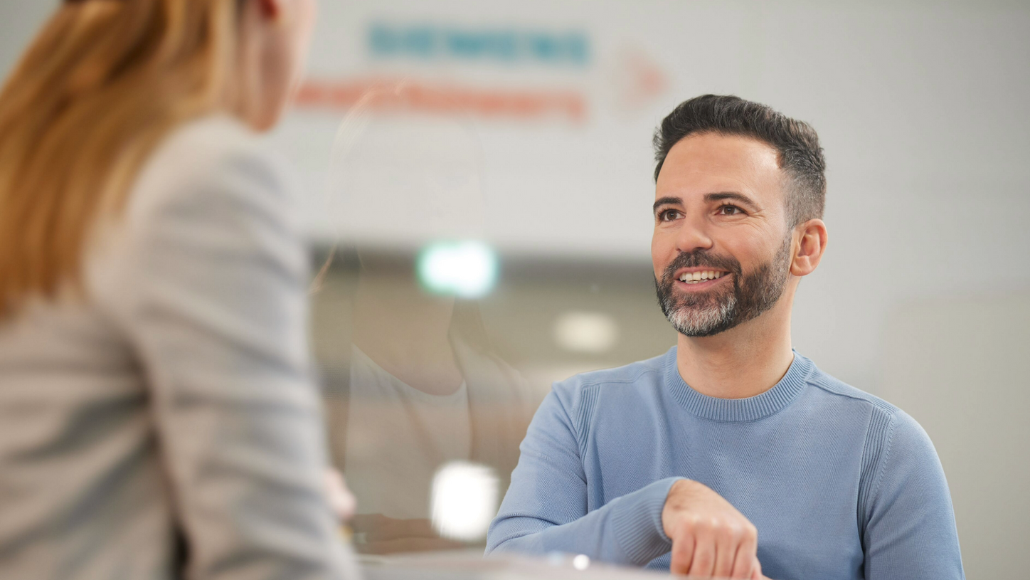 Ein Kollege lächelt im Gespräch mit einer Kollegin in der Lobby.
