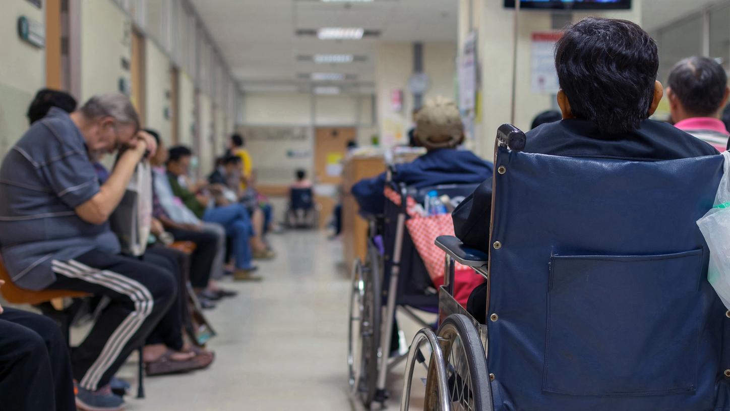A crowded hospital waiting area with patients, including individuals in wheelchairs, waiting for medical attention.