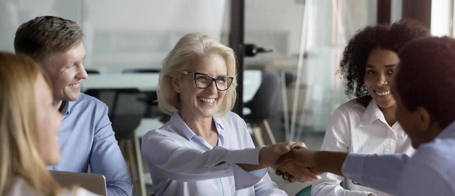 Women with grey hair smiling and shaking a colleague's hand in a meeting