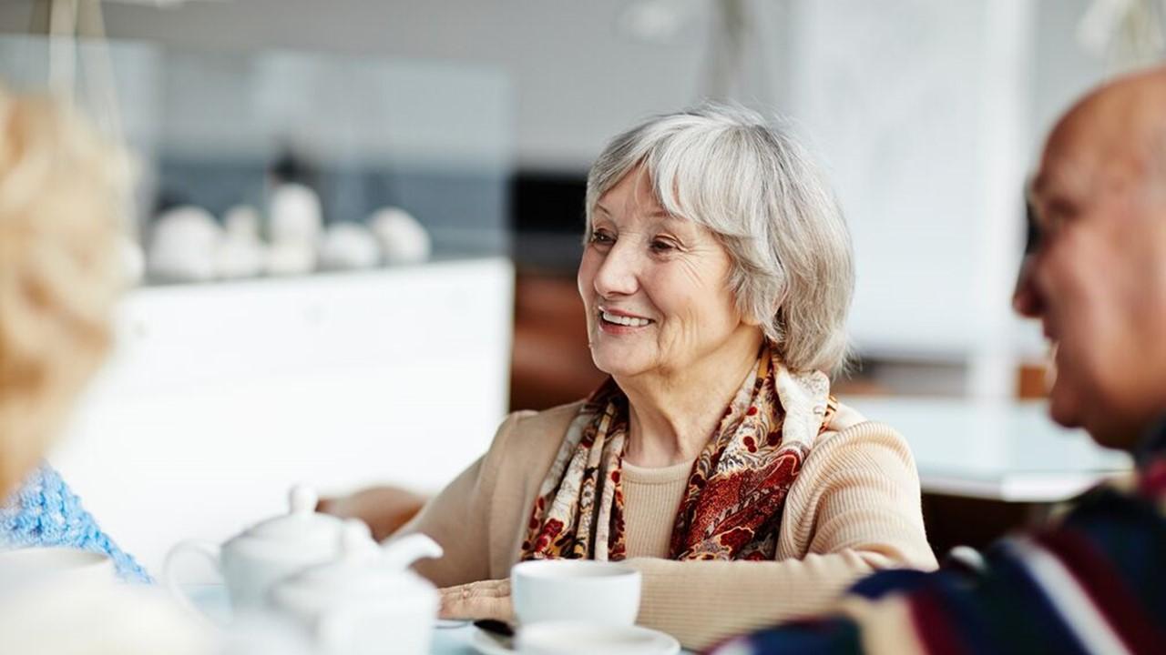 Older woman talking with others while seated at a table.