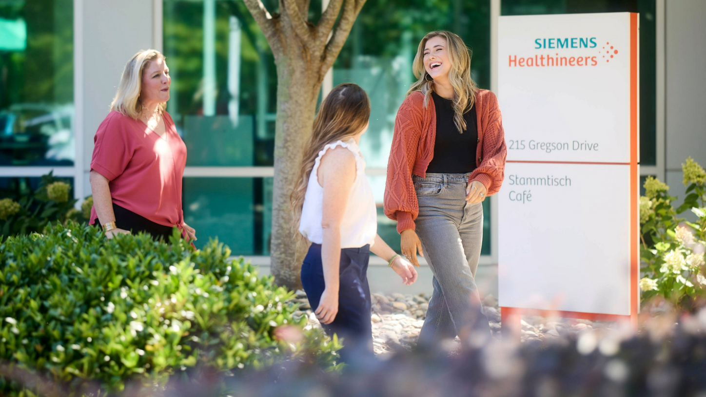 Drei Kolleginnen laufen vor einem Siemens Healthineers Büro und lachen gemeinsam.