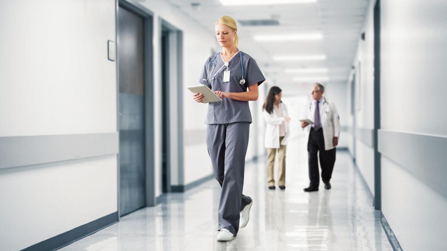 Healthcare professional using a tablet while walking through a hospital corridor.