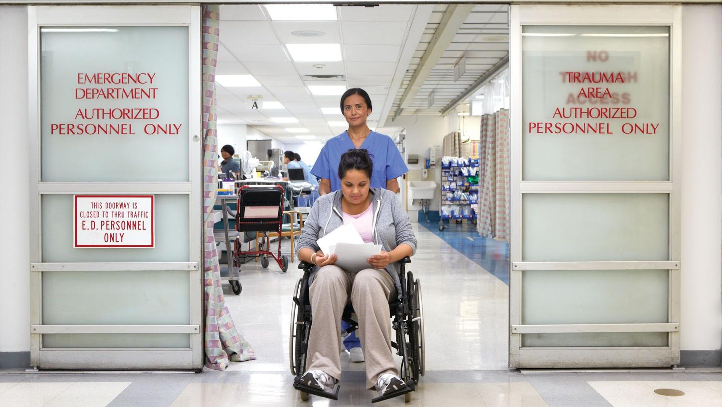 A nurse wheeling a female patient out of the Emergency Department in a wheelchair to discharge her