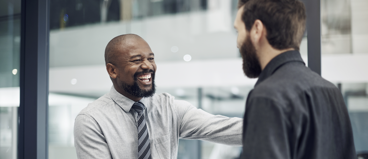 A Black man shaking hands and smiling with a white man in the office