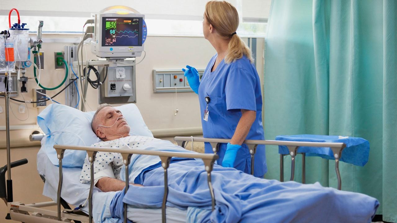 Patient in a hospital bed with a healthcare professional monitoring medical equipment.